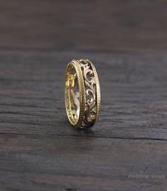 a gold wedding ring with filigrees on the inside and outside, sitting on a wooden surface