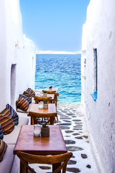 an alley way leading to the ocean with tables and chairs lined up on either side