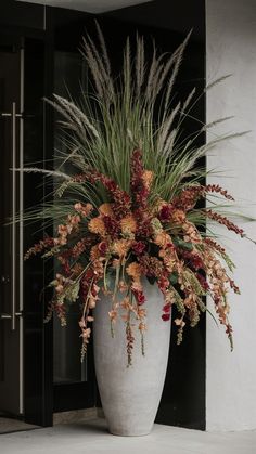 a large white vase filled with lots of different types of flowers next to a door