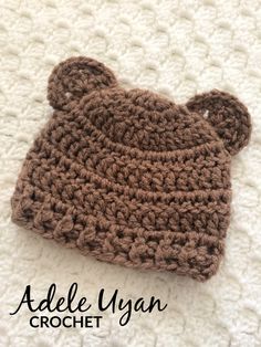 a crocheted brown bear hat laying on top of a white blanket with the ears turned down