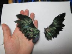 a hand holding a piece of paper with two green and black feathers attached to it