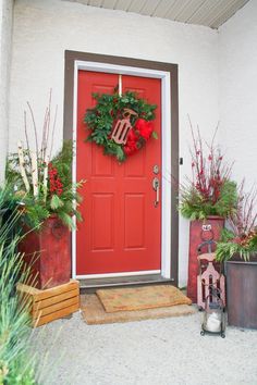 a red front door decorated with christmas wreaths and potted plants