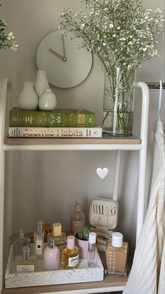 a shelf filled with cosmetics and flowers on top of a white dresser next to a clock