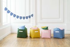 four different colored storage bags sitting on the floor in front of a window with bunting