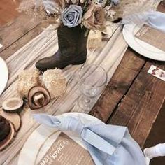 the table is set with blue napkins, silverware and brown boots on it