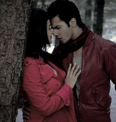 a man and woman standing next to each other near a tree with their hands on her chest