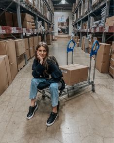 a woman sitting on top of a dolly in a warehouse