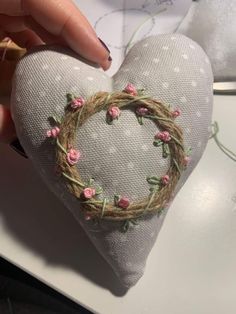 someone is holding a heart shaped pillow with flowers on the front and side, which has a wreath in the shape of a heart