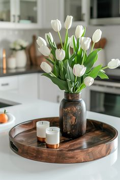 a vase filled with white flowers on top of a wooden tray next to two candles