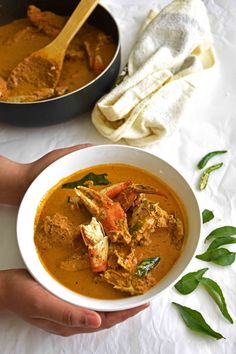 a person holding a bowl of soup with crab