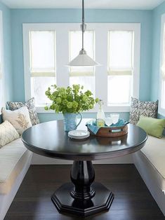 a room with blue walls and wooden flooring has a table, bench, and two windows