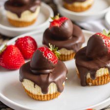 chocolate covered cupcakes and strawberries on a white plate with other dessert items in the background