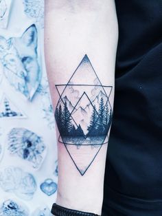 a man's arm with a mountain and pine trees tattoo on the left forearm