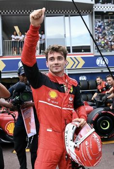 a man in a red racing suit waves to the crowd while holding his fist up