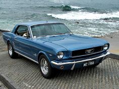 an old mustang is parked on the side of the road next to the ocean with waves in the background