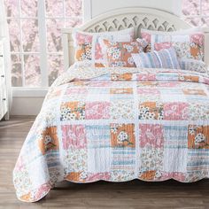 a bed covered in a colorful patchwork quilt next to a white headboard and window