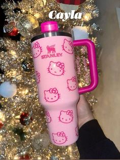 a person holding a pink hello kitty water bottle in front of a christmas tree