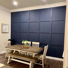 a dinning room table and bench in front of a blue paneled wall