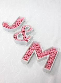 the letters m and w are made out of pink candy beans on a white surface