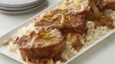 some meat and rice on a white plate with silver ware in the backgroud