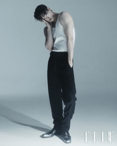 a man in black pants and white shirt standing with his head on his hand while talking on the phone