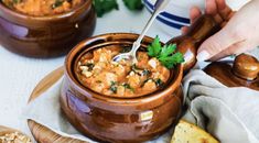 a person is spooning into a bowl of soup with bread and parsley on the side