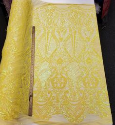 a piece of yellow fabric with gold sequins on it next to a ruler