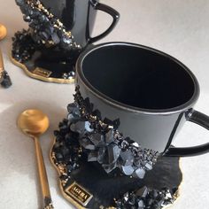 two black coffee cups and spoons on a white tablecloth with gold trimming