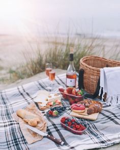 a picnic with bread, fruit and wine on a blanket at the beach in front of the ocean