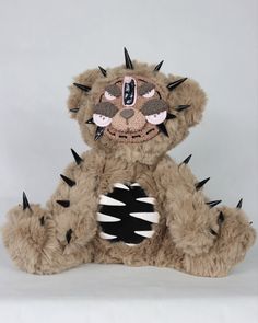 a brown teddy bear with spikes on its face and chest sitting down in front of a white background