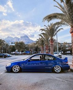 a blue car parked on the side of a road next to palm trees and mountains