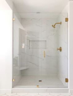 a white bathroom with gold fixtures and marble tile flooring on the shower stall door