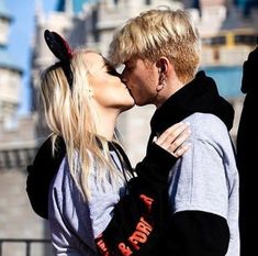 a man and woman kissing each other in front of a castle with buildings behind them