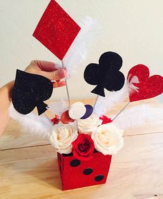 someone is holding up some paper hearts and playing cards in a vase with flowers on the table