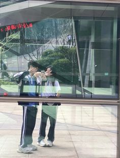 two people standing in front of a glass building with their hands up to each other