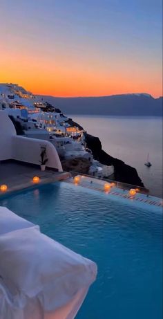 an outdoor swimming pool with candles lit at night overlooking the sea and town in the distance