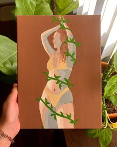 a painting of a woman with green leaves on her body is being held up by a hand