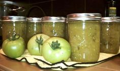 several jars filled with different types of food on a counter top next to tomatoes and peppers