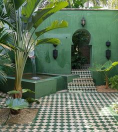 an outdoor courtyard with green walls and checkered tile flooring, potted plants on either side