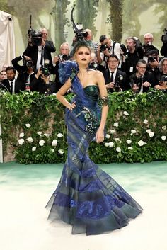 a woman in a blue and black gown standing on a white floor with cameras around her