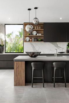 a modern kitchen with marble counter tops and black cabinets, along with two bar stools