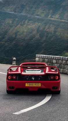 the rear end of a red sports car driving on a road with mountains in the background