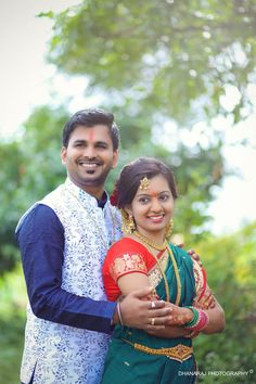 a man and woman standing next to each other in front of some trees with their arms around each other