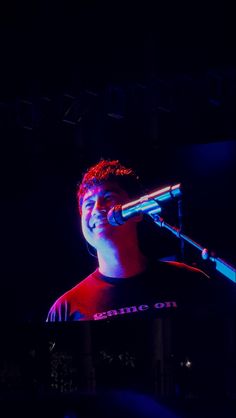 a man singing into a microphone at a concert in the dark with his eyes closed