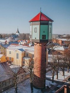 a tall tower with a red top in the middle of snow covered ground next to buildings