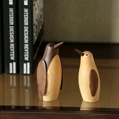 two small wooden birds sitting on top of a table next to some bookcases