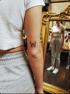 a woman with a butterfly tattoo on her left arm, standing in front of a mirror