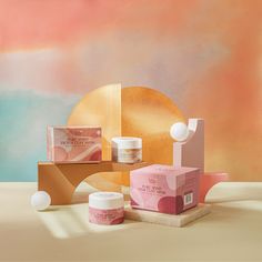 an assortment of skin care products sitting on a table with a pink and yellow background