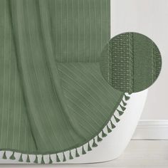 a green shower curtain with white trim and tassels on the bottom, along with a round hole in the middle