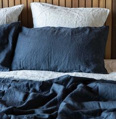 an unmade bed with blue linens and pillows on the headboard, in front of a wood paneled wall